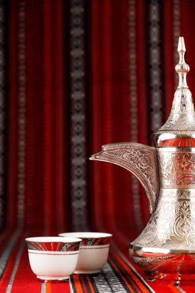 Arabian tea cups and a dallah are placed on traditional red fabric